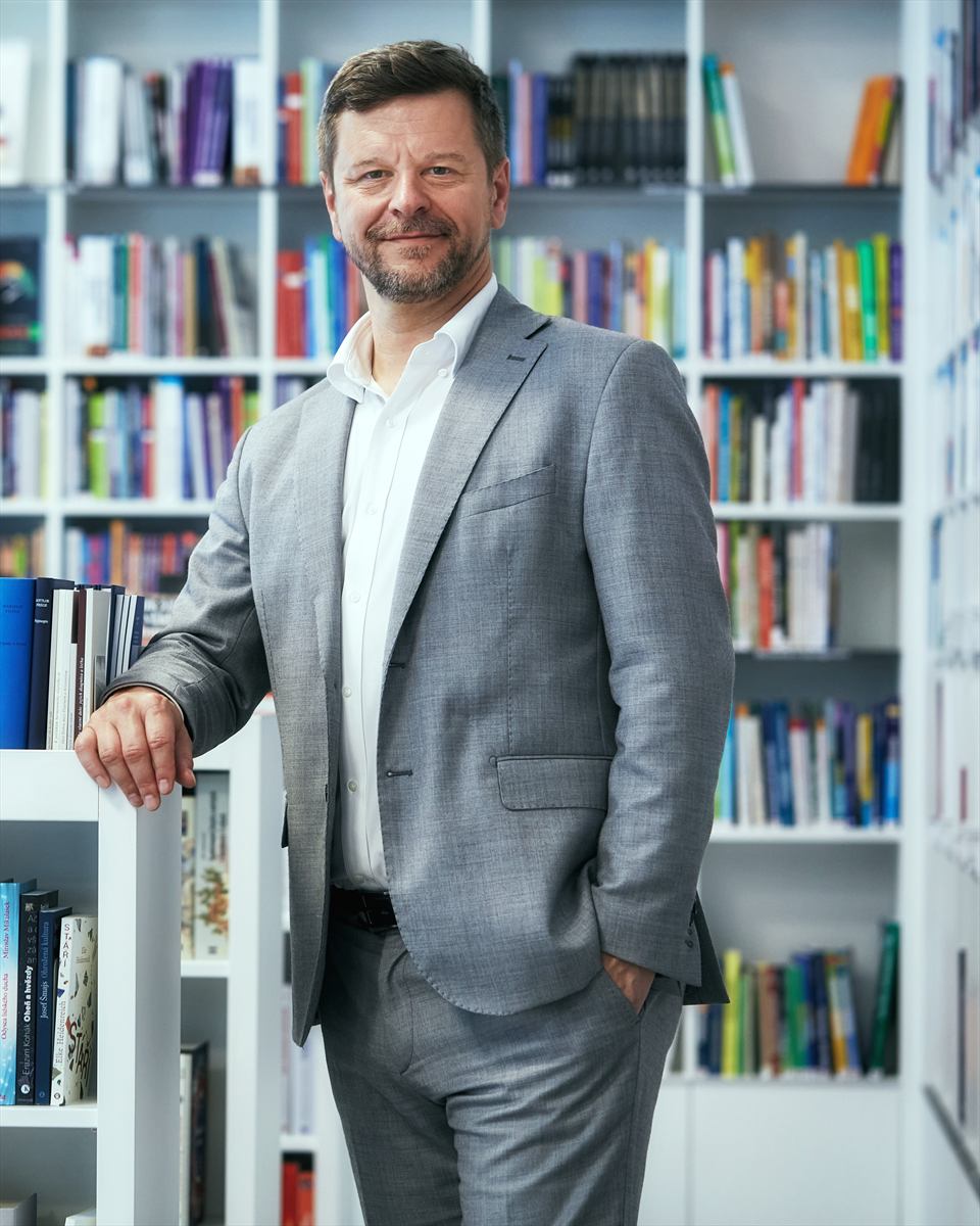 Petr Kopecký stojí v univerzitním knihkupectví před bílými regály s barevnými knihami.