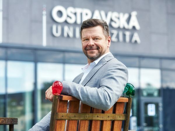 Petr Kopecký sedí na lavičce před budovou Ostravské univerzity.