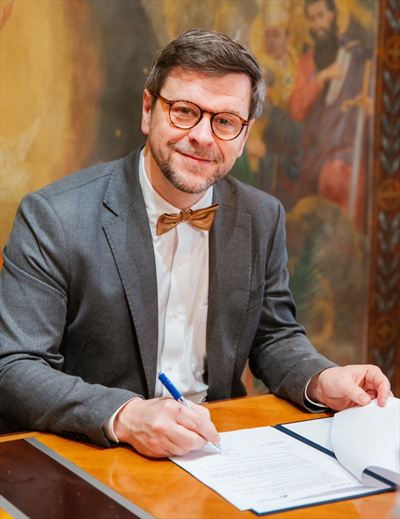 Petr Kopecký podepisuje dokument u stolu v historickém sále.